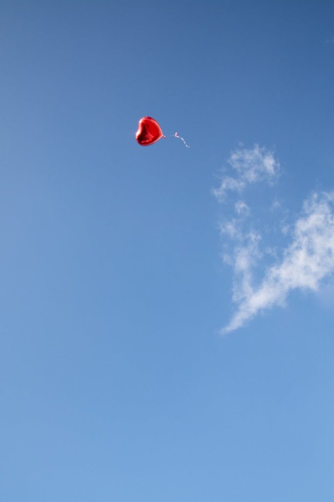 Red heart balloon floating in the sky with a heart cloud.