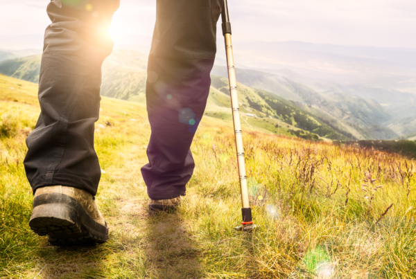 Person walking on grassy path with assistance. Light shining in background.