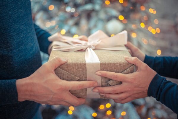 two sets of hands holding a gift with a whit ribbon. Gives the appearance of Gift Giving