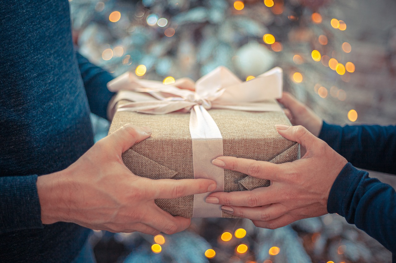 two sets of hands holding a gift with a whit ribbon. Gives the appearance of Gift Giving