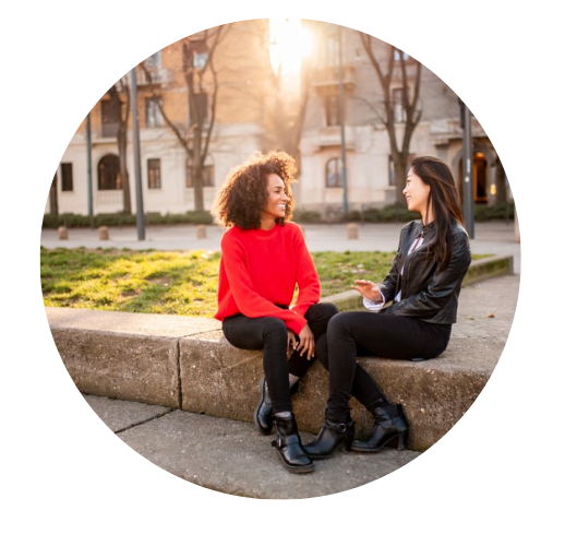 Two women talking and enjoying each others company outside while the sun sets behind a building adding beautiful light.