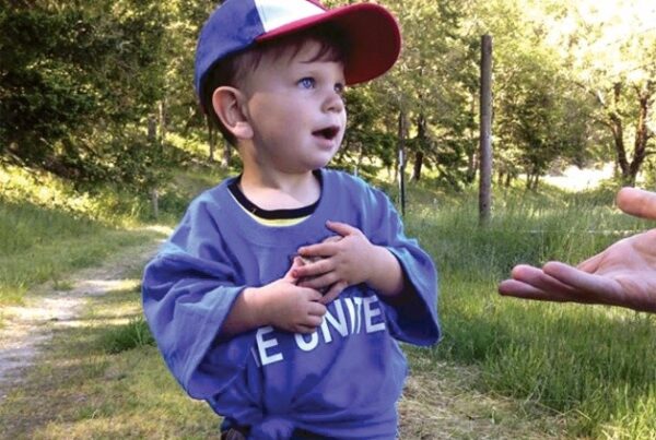 Little boy in a grassy field and someone is reaching out their hand.