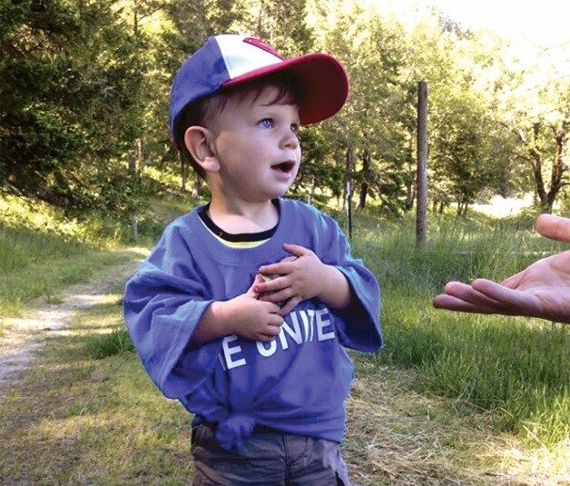 Little boy in a grassy field and someone is reaching out their hand.