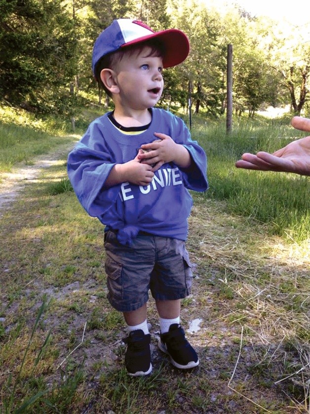 Little boy in a grassy field and someone is reaching out their hand.